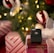 A black wireless payment terminal by Vagaro is placed on a wrapped gift box with a white mesh bow. The background features a decorated Christmas tree with illuminated lights and ornaments in red, white, and green colors.
