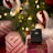 A black wireless payment terminal by Vagaro is placed on a wrapped gift box with a white mesh bow. The background features a decorated Christmas tree with illuminated lights and ornaments in red, white, and green colors.